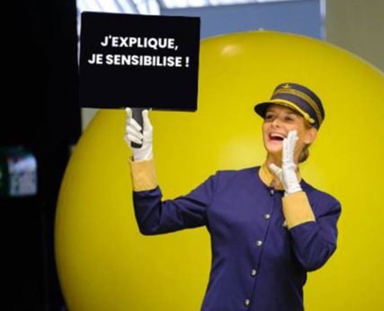 Image d’un crieur sur salon avec un panneau « j’explique, je sensibilise »