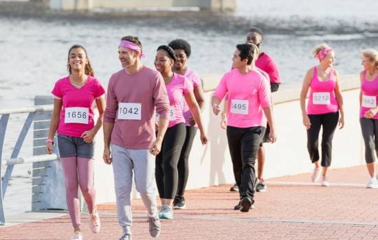Participants vêtus de rose marchant sur un parcours en bord de rivière lors d’une course ou marche de sensibilisation au cancer du sein.