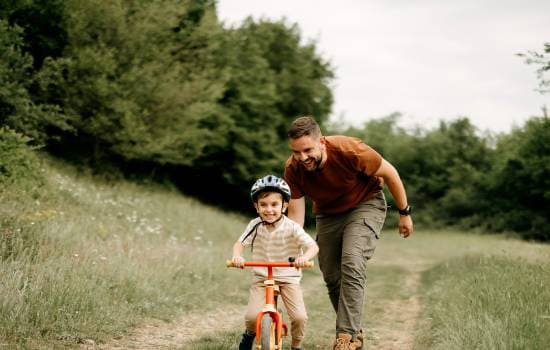 Enfant à vélo sur un chemin naturel accompagné d’un adulte, dans un environnement verdoyant.
