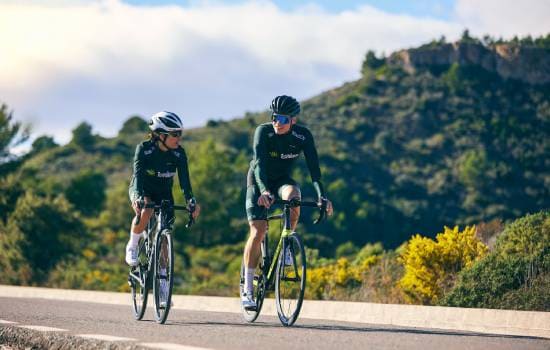 Deux cyclistes sur route roulant dans un paysage vallonné et verdoyant lors d’une sortie sportive en plein air.