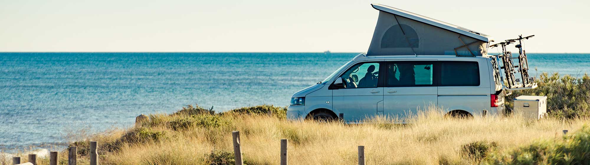 Une tente perchée au dessus d'un camping car sur une plage