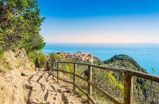 Sentier de randonnée côtier bordé de végétation, avec vue sur la mer et le village de Corniglia dans les Cinque Terre, Italie.