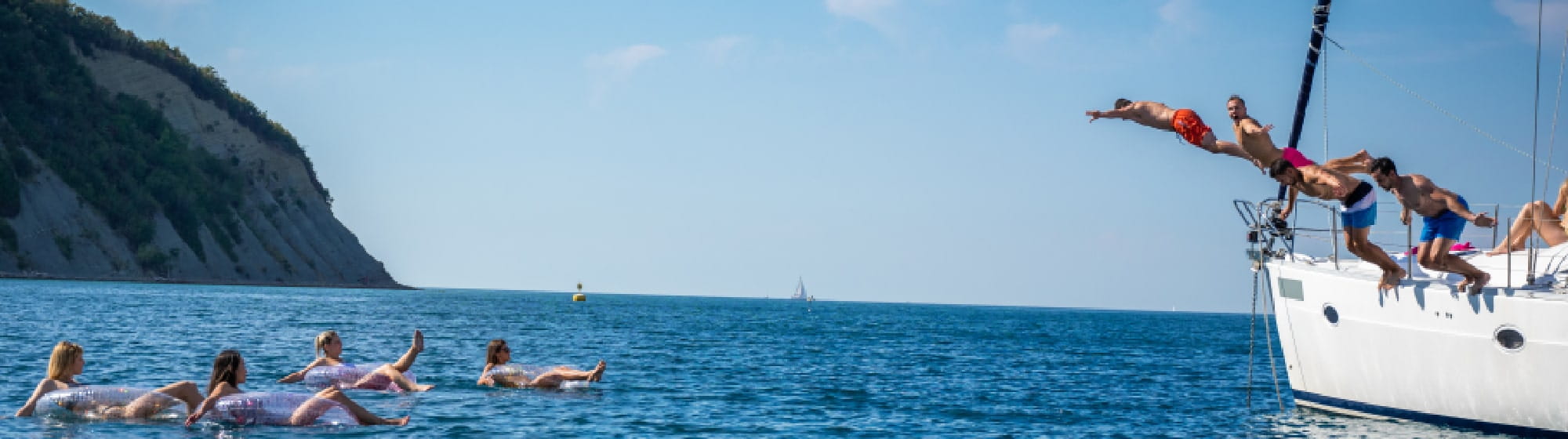 Des jeunes sottant d'un voilier pour rejoindre leurs amis dans l'eau sur dses bouées flottantes. 
