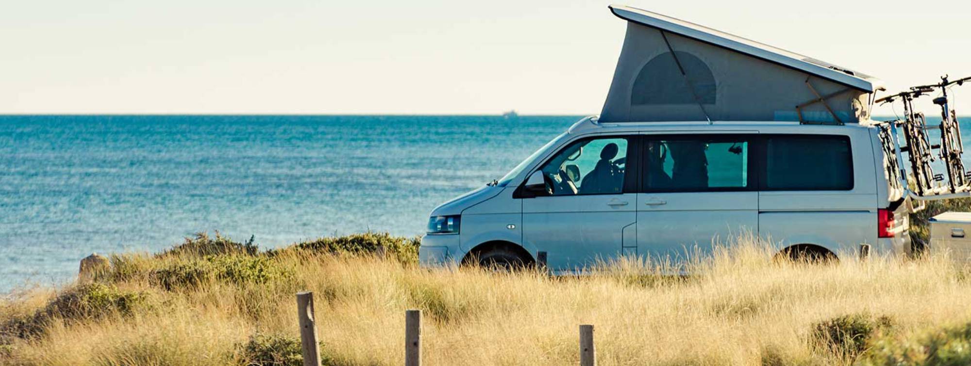 Une tente perchée au dessus d'un camping car sur une plage
