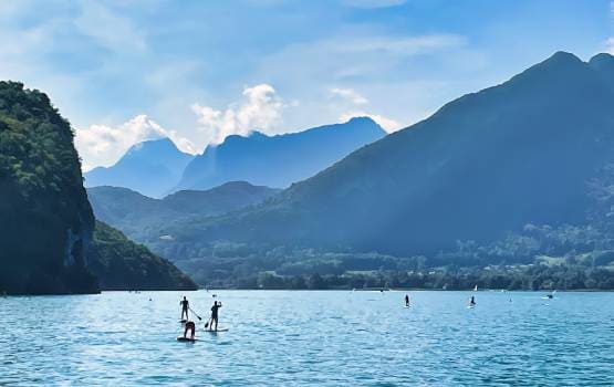 Un lac entouré de montagne avec des personnes pratiquants du paddle