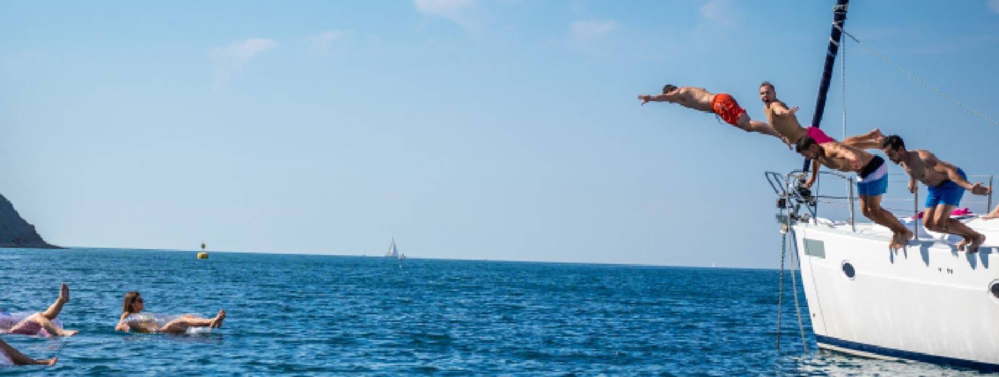 Des jeunes sottant d'un voilier pour rejoindre leurs amis dans l'eau sur dses bouées flottantes. 