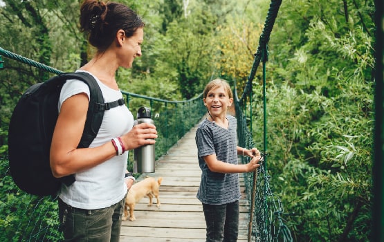 Une femme et un enfant sur un pont protégé avec des cordes de sécurité en pleine forêt. 