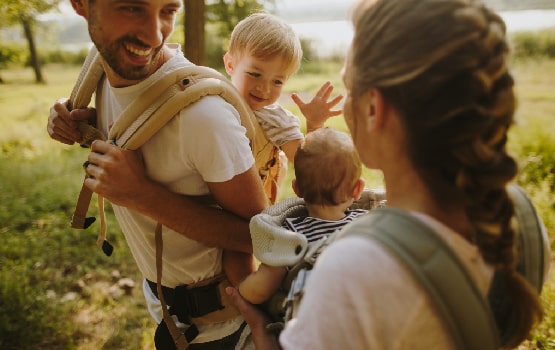 Une famille avec deux adultes portant chacun un enfant sur leur dos. 