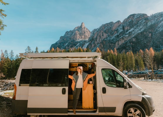 Une femme devant son van avec en fond la montagne